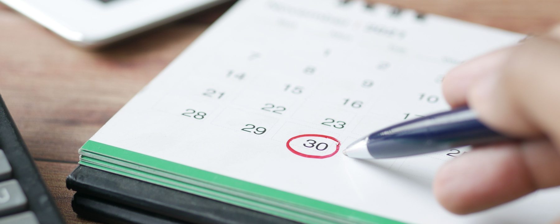 Eine Hand markiert einen Tag im Monatskalender