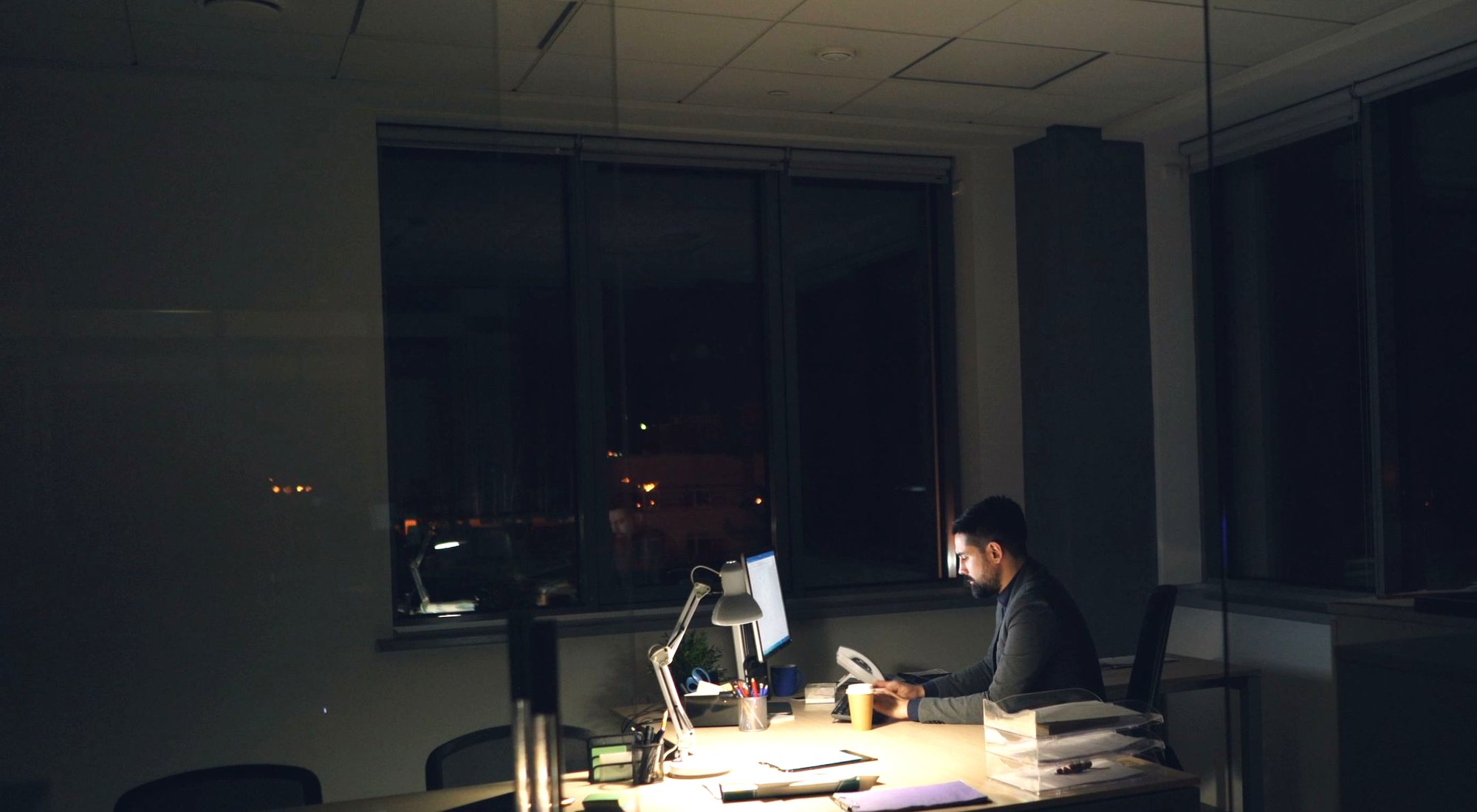 Ein beleuchtetes Büro bei Nacht, an einem Schreibtisch sitzt noch jemand