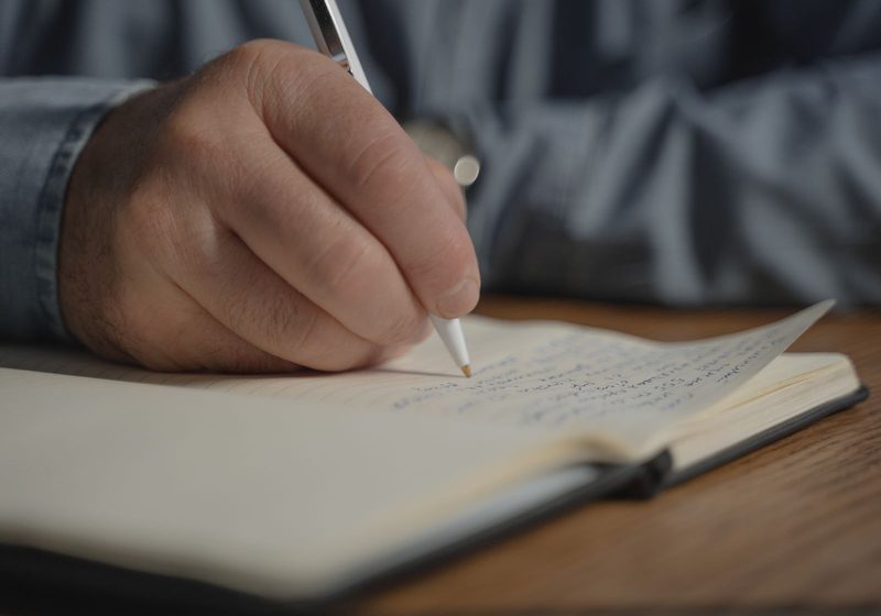 Eine Hand schreibt mit dem Stift in ein Notizbuch