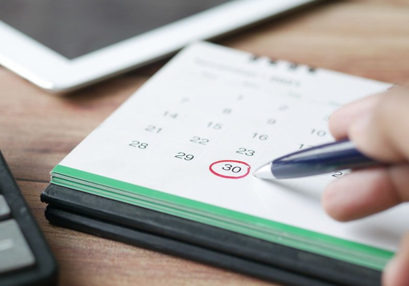 Eine Hand markiert einen Tag im Monatskalender